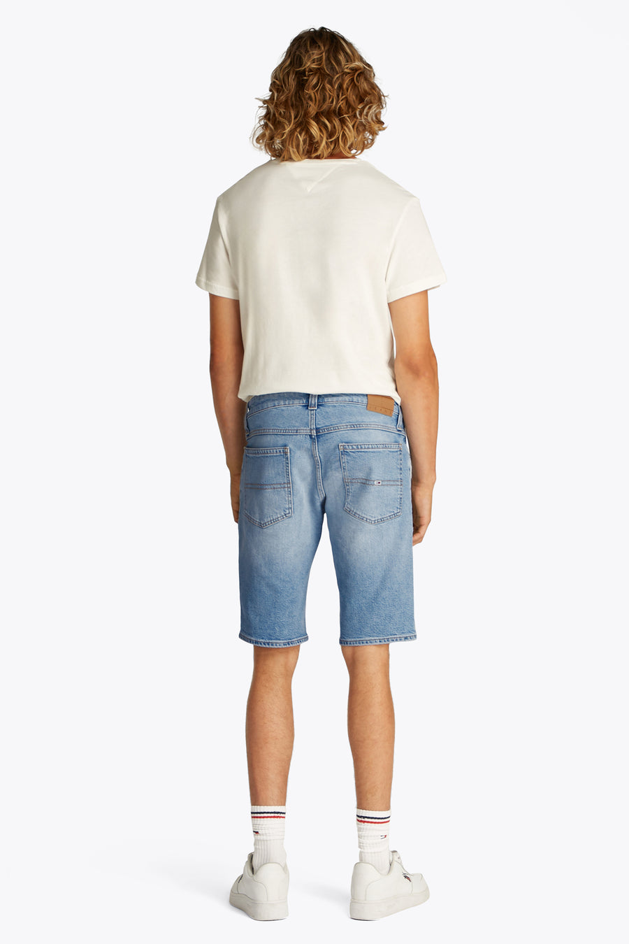 Shorts de denim bleu clair de TOMMY JEANS, vu de l'arrière avec des sneakers blanches et des chaussettes rayées.
