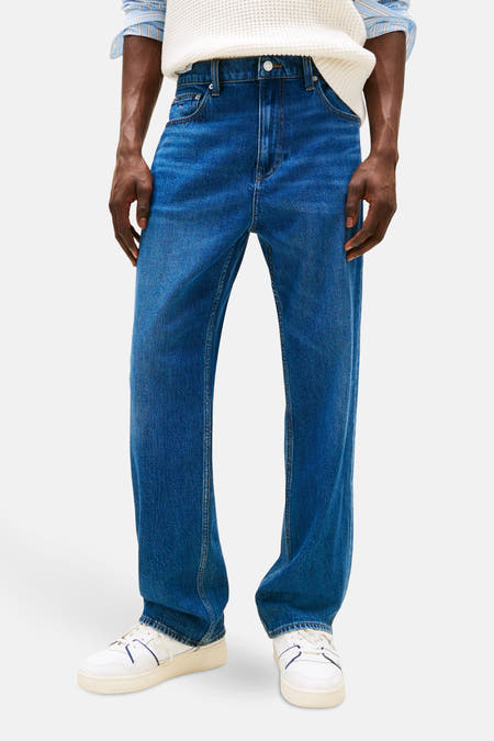 Jean droit en denim bleu marine de TOMMY JEANS, porté avec un pull tricoté et des baskets blanches.