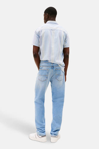 Jean droit bleu clair de TOMMY JEANS, avec des poches classiques et porté avec un chemise à carreaux et des baskets blanches.
