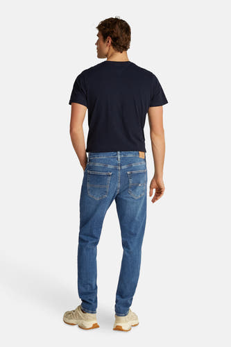 Jean en denim bleu clair tapered de TOMMY JEANS, avec des poches arrière et des baskets beige.