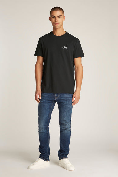 T-shirt noir à manches courtes de TOMMY JEANS, porté avec des jeans bleus foncés et des baskets blanches.