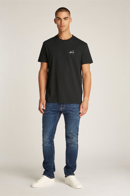T-shirt noir à manches courtes de TOMMY JEANS, porté avec des jeans bleus foncés et des baskets blanches.