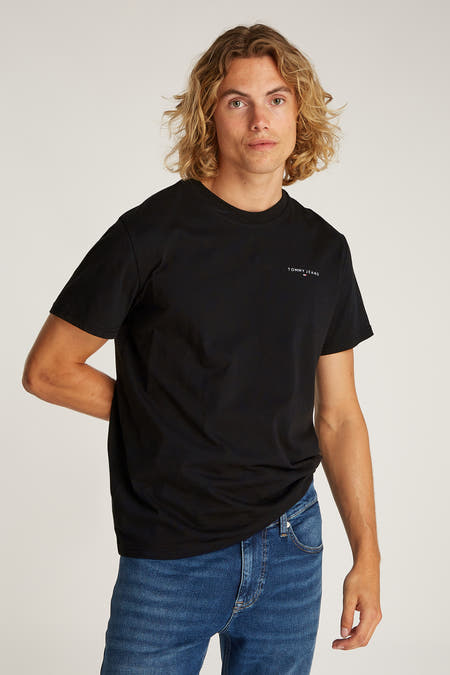 T-shirt noir à manches courtes de TOMMY JEANS, porté avec des jeans bleus et des baskets blanches.