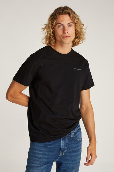T-shirt noir à manches courtes de TOMMY JEANS, porté avec des jeans bleus et des baskets blanches.