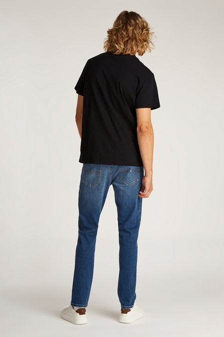 T-shirt noir à manches courtes de TOMMY JEANS, vu de dos avec des jeans bleus et des baskets blanches.