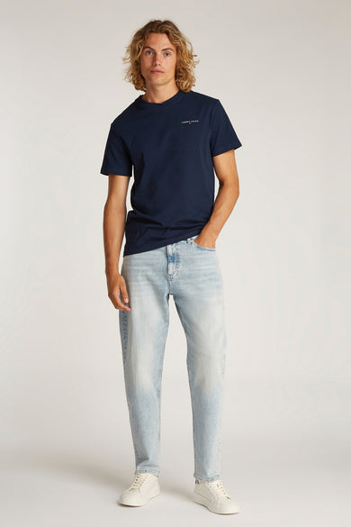 T-shirt bleu à manches courtes de TOMMY JEANS, porté avec des jeans bleus clairs et des baskets blanches.