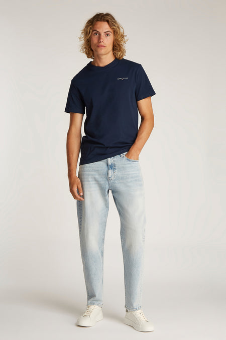 T-shirt bleu à manches courtes de TOMMY JEANS, porté avec des jeans bleus clairs et des baskets blanches.
