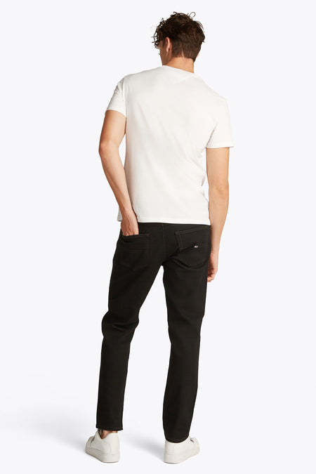 T-shirt blanc à manches courtes de TOMMY JEANS, vu de l'arrière avec une main dans la poche.