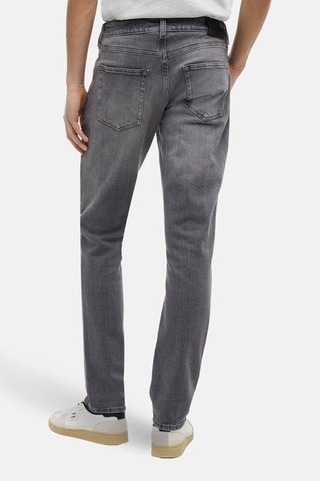 Jeans slim en denim gris foncé de TOMMY JEANS, vue de dos, avec délavage subtil et chaussures décontractées.
