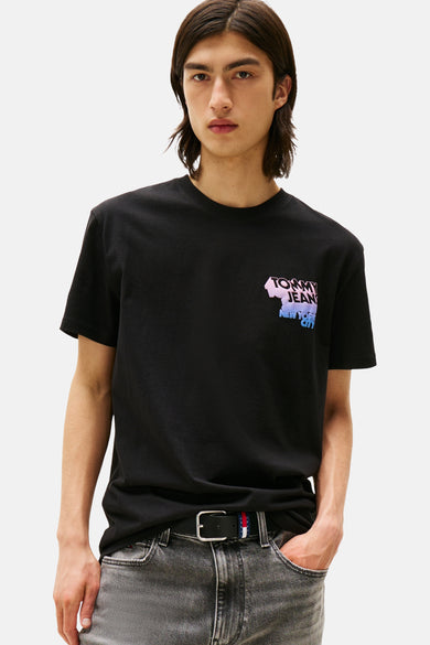 T-shirt noir à manches courtes de TOMMY JEANS, avec une impression sur la poitrine, associé à un jean gris et une ceinture noire.