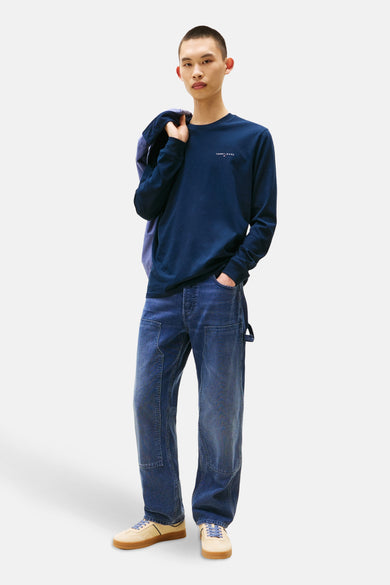 T-shirt bleu à manches longues de TOMMY JEANS, avec un manteau sur l'épaule et un pantalon en denim.