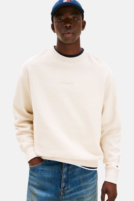 Gilet beige de TOMMY JEANS, texture rayée et détail de logo subtil dans le col, porté avec des jeans et des baskets.