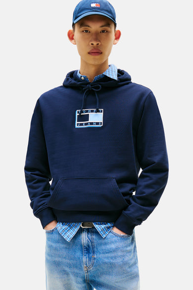 Pull-over bleu avec capuche de TOMMY JEANS, vu de dos, avec des shorts en denim, des chaussettes blanches et des baskets.