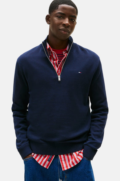 Pull-over bleu avec col montant de TOMMY JEANS, porté avec un chemisier rayé et des jeans larges.