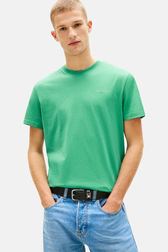 T-shirt vert à manches courtes de TOMMY JEANS, avec un col rond et porté avec un jean ample et des baskets blanches.