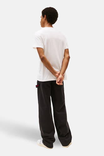 T-shirt blanc à manches courtes de TOMMY JEANS, dos t la caméra, associé à un pantalon noir.