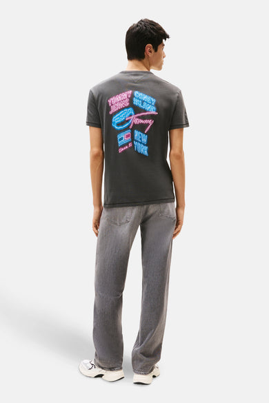 T-shirt gris à manches courtes de TOMMY JEANS, avec une impression inspirée par le néon sur l'arrière, associé à des jeans gris et des baskets blanches.