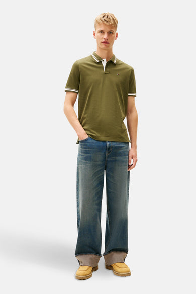 Kaki polo avec des manches courtes de TOMMY JEANS, avec des rayures blanches sur le col et les manches, associé à des jeans larges.