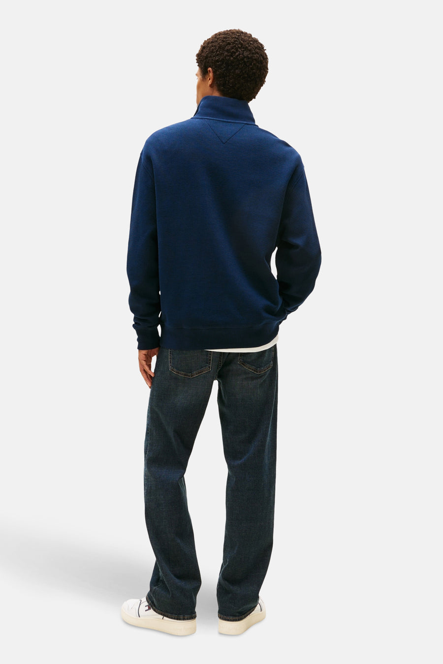 Pull-over bleu de TOMMY JEANS, avec des manches longues, sur un modèle avec des jeans et des baskets blanches.