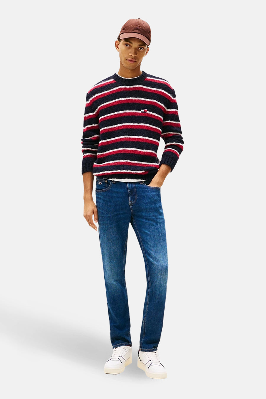 Slim fit jeans van TOMMY JEANS in donkerblauwe denim, gecombineerd met een gestreepte trui en een pet.
