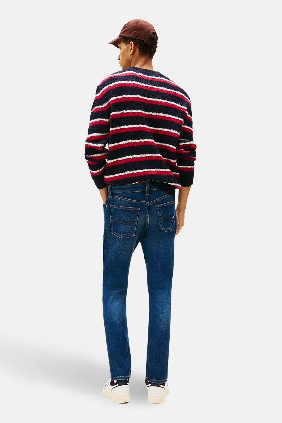 Blauwe slim fit jeans van TOMMY JEANS, met een donkere wassing, gedragen met een gestreepte trui en pet.