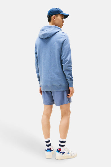 Pull-over bleu avec capuche de TOMMY JEANS, associé à des shorts coordonnés, des chaussettes rayées et des baskets blanches.