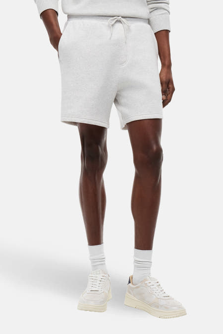 Grijze short van TOMMY JEANS, met trekkoord en gedragen met witte sokken en crèmekleurige sneakers.
