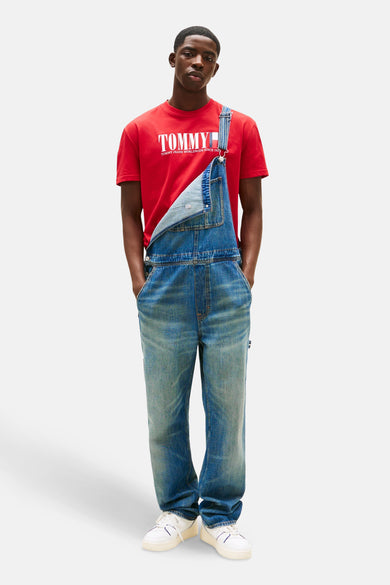 T-shirt rouge à manches courtes de TOMMY JEANS, porté sous un short en jean bleu et des baskets blanches.