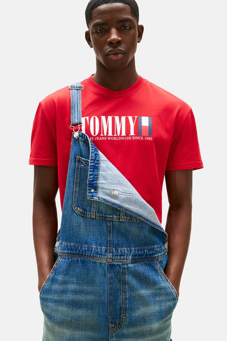T-shirt rouge à manches courtes de TOMMY JEANS, porté avec un short en denim les mains dans les poches.