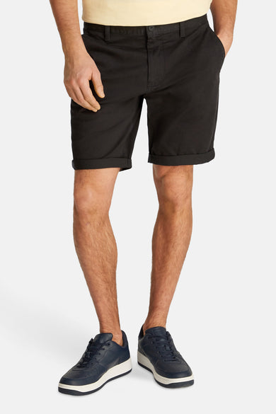 Short noir de TOMMY JEANS, avec des poches pliées et porté avec des baskets bleues.