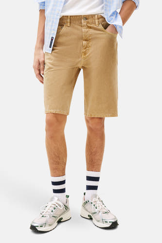 Jean short beige de Tommy Jeans, avec des poches rabattues et des chaussettes rayées avec des sneakers.