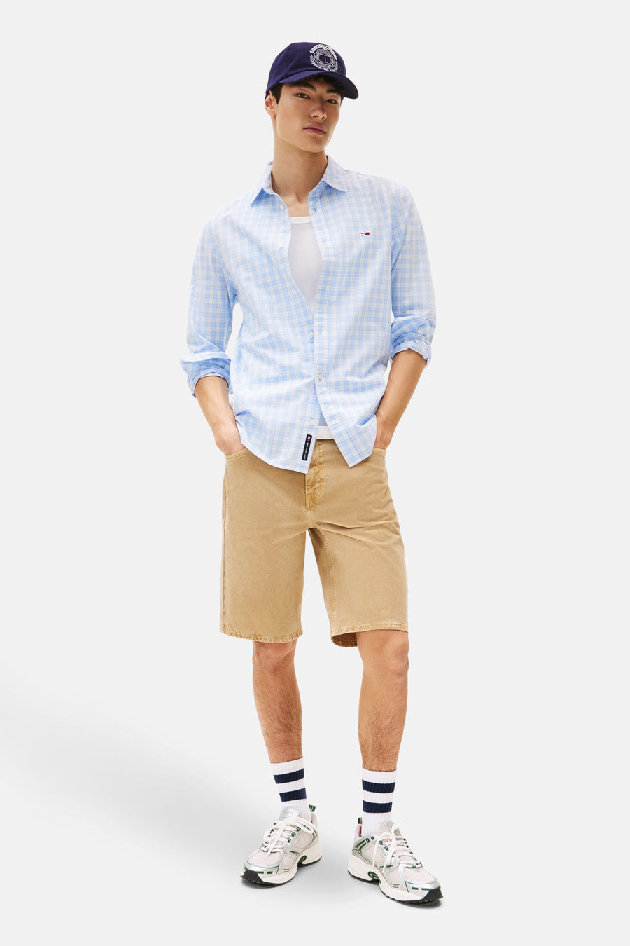 Jean short beige Tommy Jeans avec une blouse bleue claire à carreaux et un chapeau bleu marine.