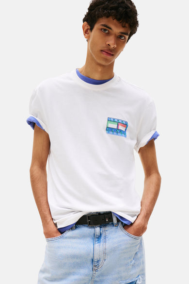 T-shirt blanc à manches courtes de TOMMY JEANS, avec des détails bleus au col et aux manches, et un logo distinctif sur la poitrine.