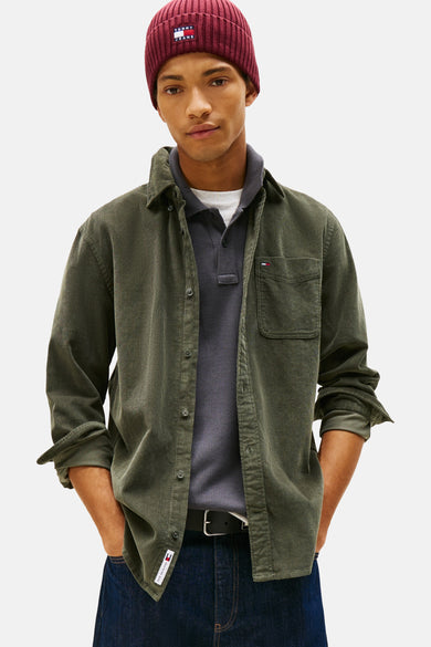 T-shirt vert de TOMMY JEANS, avec des manches longues, porté avec un chapeau bordeaux et des jeans bleus foncés.
