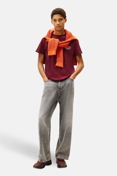 T-shirt rouge à manches courtes de TOMMY JEANS, avec une veste orange nouée nonchalamment sur les épaules.