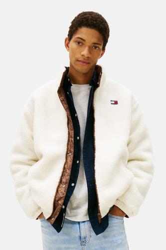 Manteau court couleur crème de TOMMY JEANS, avec des détails marrons et porté sur un chemisier bleu et un T-shirt gris.