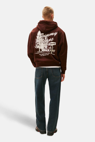 Achterkant van een man met een bruine hoodie met witte print, blauwe jeans en sportschoenen op een witte achtergrond.