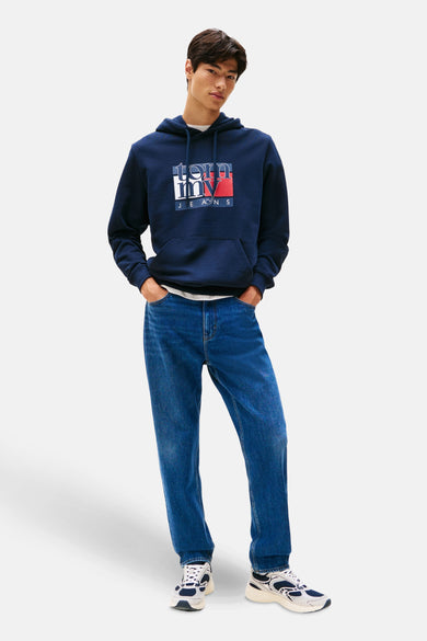 Pull-over bleu avec capuche de TOMMY JEANS, avec un logo sur la poitrine, associé à des jeans bleus et des baskets blanches.