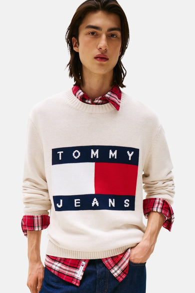 T-shirt écru de Tommy Jeans avec un col rond, portant une impression de logo rectangulaire et porté sur un chemisier rayé rouge.