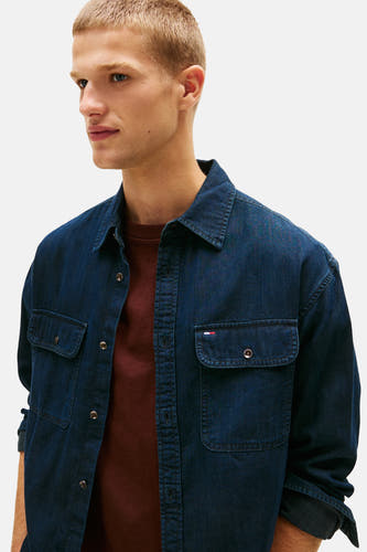 Chemise en jeans bleu marine de TOMMY JEANS, avec des poches sur la poitrine et portée sur une chemise rouge bordeaux.