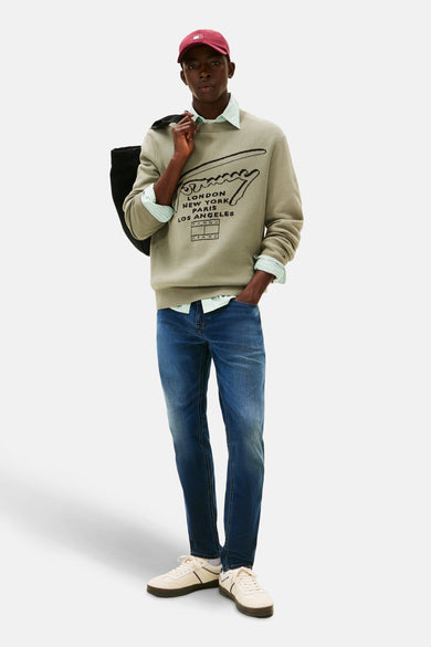 Jean tapered bleu marine de TOMMY JEANS, associé à un pull et des baskets blanches pour un look décontracté.