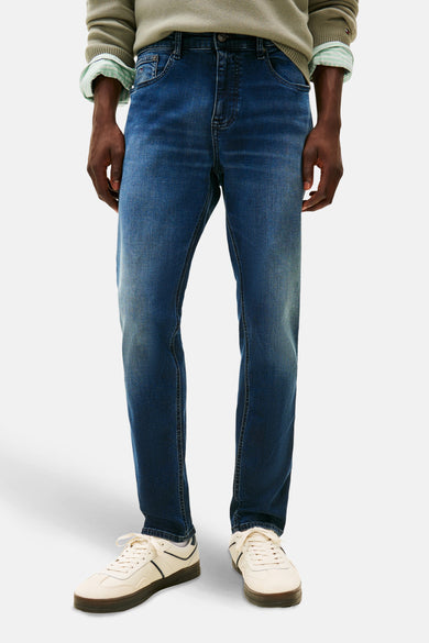 Jean tapered bleu marine de TOMMY JEANS, avec des baskets décontractées et un pull vert.