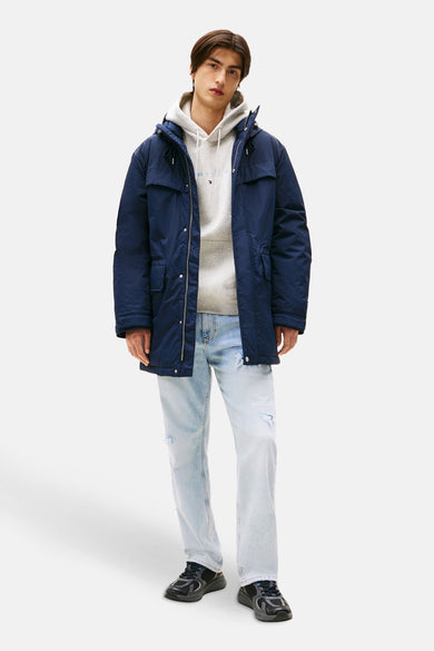 Long manteau bleu de TOMMY JEANS, porté sur un pull gris et des jeans bleus clairs déchirés.