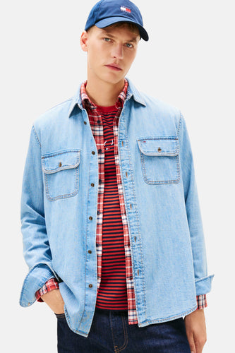 Man met een blauwe Tommy Jeans pet, denim overhemd, rood geruit overhemd en gestreepte trui.