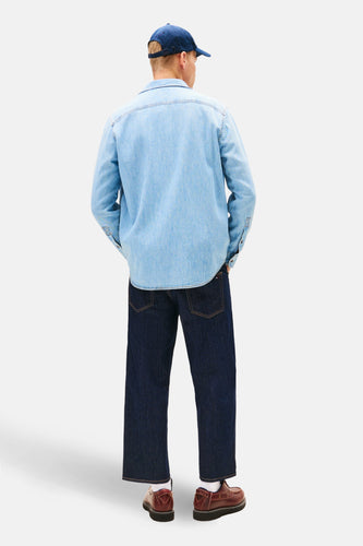 Man van achteren, blauwe denim overhemd en jeans, bruine schoenen, blauwe pet.
