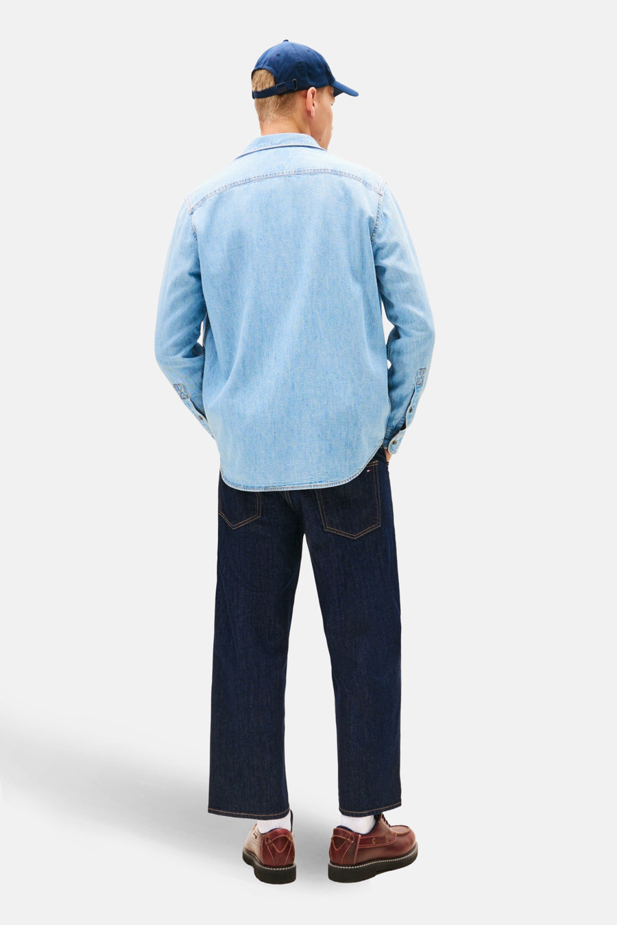 Man van achteren, blauwe denim overhemd en jeans, bruine schoenen, blauwe pet.
