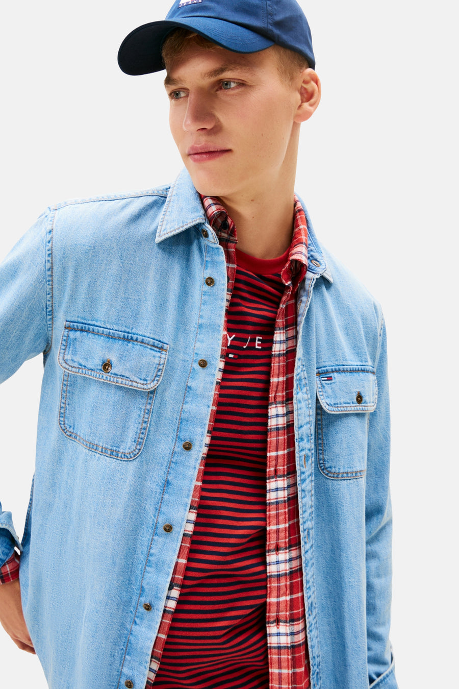 Man met blauwe pet, denim overhemd, geruit overhemd en gestreepte T-shirt.