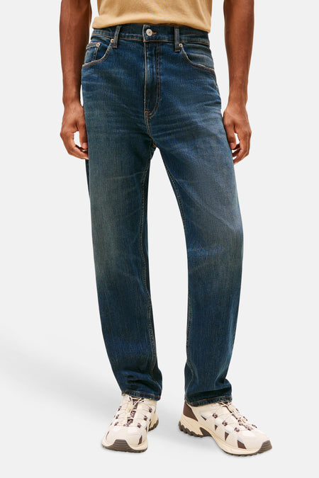 Een man in blauwe spijkerbroek en crèmekleurige sneakers.