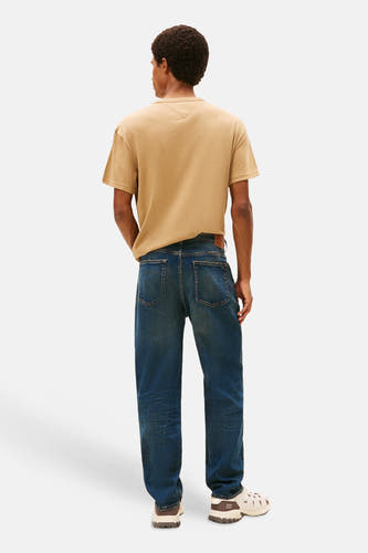 Jean tapered en denim bleu marine de TOMMY JEANS, avec une ceinture en cuir marron et des chaussures crème.