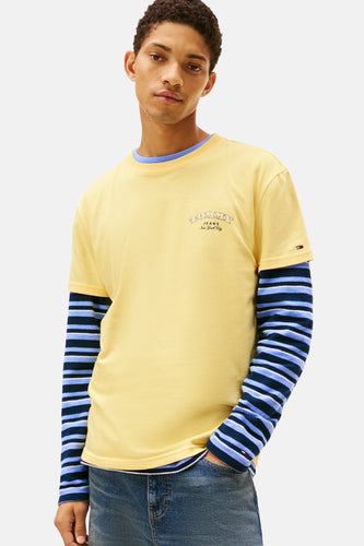 Jonge man draagt gele T-shirt met lange mouwen met blauwe strepen en blauwe spijkerbroek.